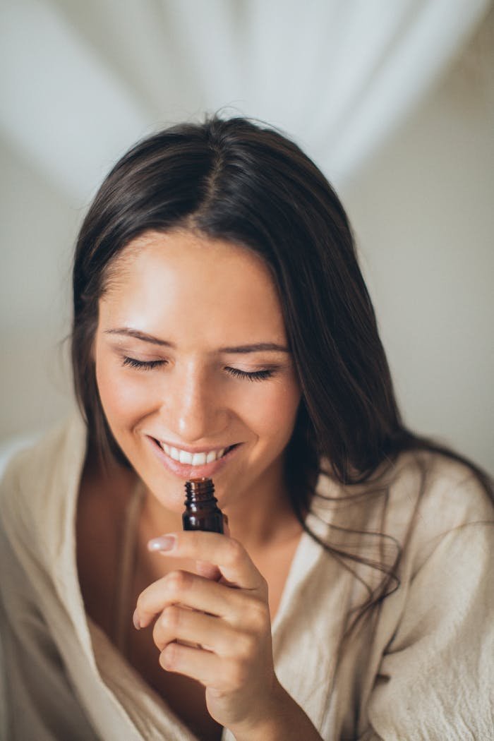 why-choose-us-02 A smiling woman with closed eyes enjoying the scent from a glass bottle, highlighting a moment of relaxation and aroma therapy.